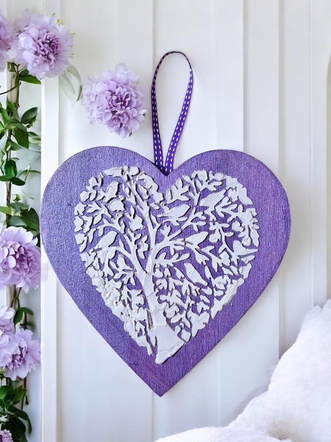 Uma tela em forma de coração, pintada em lilás e com uma árvore modelada em pasta e pintada à mão. Uma peça que celebra as raízes, o tempo e o que vai crescendo com amor. Tamanho: 18cm x 19cm Valor: 10€